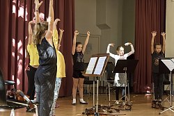 In einem Raum der Städtischen Musikschule stehen Mädchen im Halbkreis an Notenständern. Auf dem Bioden sind Geigen abgelegt. Die Mädchen strecken ihre Arme in die Luft.